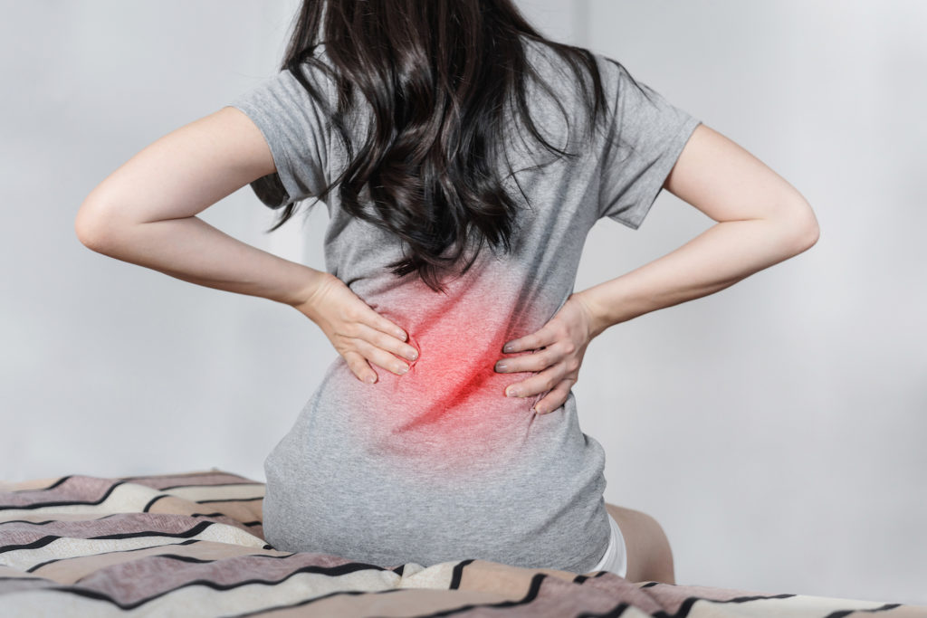 young woman sitting beside the bed holding her lower back pain