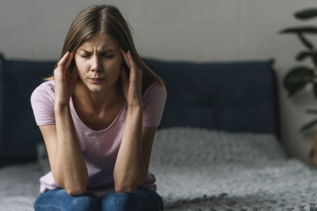 woman wearing pink shirt sitting in a couch suffer from headache