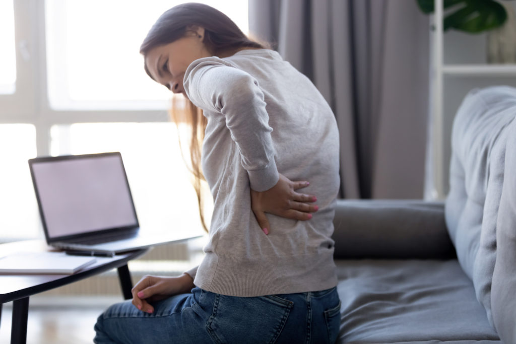 woman sitting in a couch holder her lower back pain