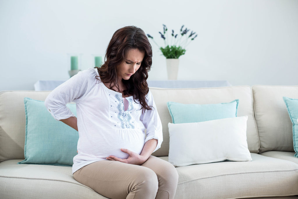 pregnant woman sitting in a couch holding her baby bump and lower back